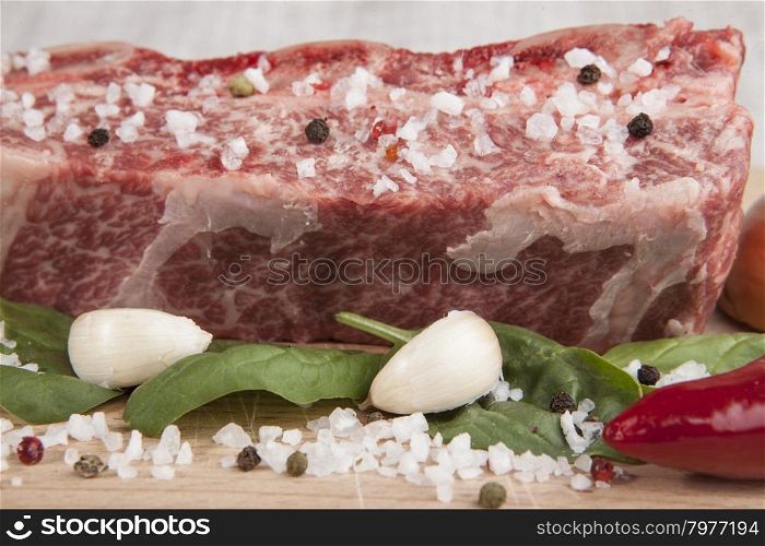 Close-up piece of fresh marbled beef, chili pepper, parsley, onion, garlic, ribs lie on a wooden tray.