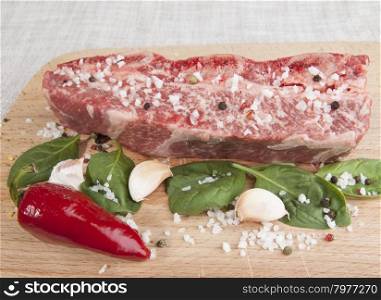 Close-up piece of fresh marbled beef, chili pepper, parsley, onion, garlic, ribs lie on a wooden tray.