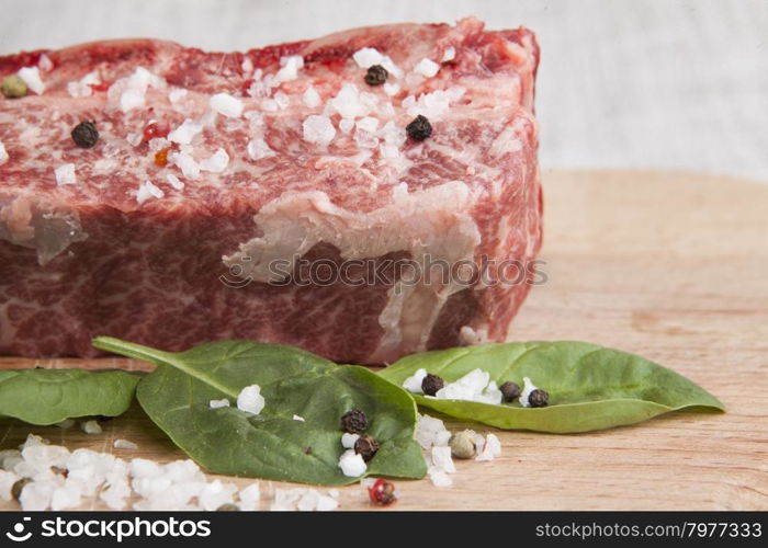 Close-up piece of fresh marbled beef, chili pepper, parsley, onion, garlic, ribs lie on a wooden tray.