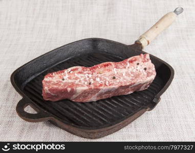 Close-up piece of fresh marbled beef with sea salt and black pepper, on a cast-iron grill pan.