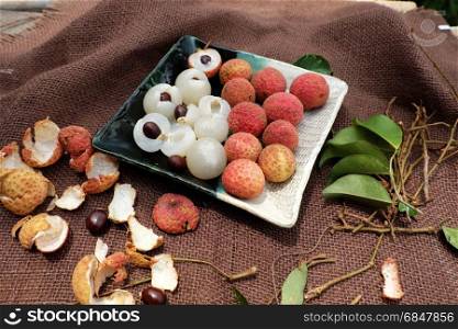 Close up plate of fruit on brown background, litchi or lychee fruits or Vai thieu. Red fruit peel with juicy pulp in white that sweet and delicious