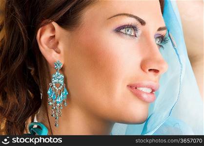 close up portrairt of a pretty brunette with blue-sky earring playing to hide her face with a summer headscarf