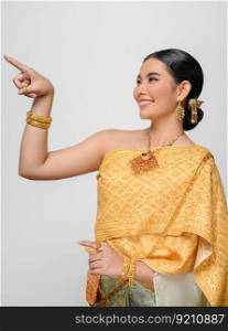 Close up, Portrait beautiful Asian woman in traditional Thai dress costume smile and point her finger with gracefully pose  on white background, copy space