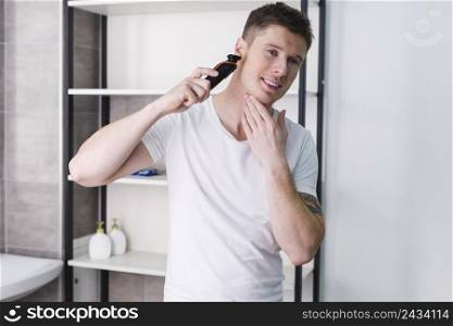 close up portrait happy man looking camera shaving his face with electric razor