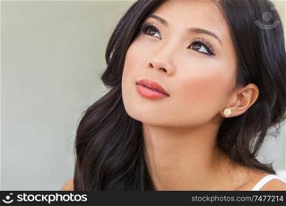 Close up portrait of a beautiful thoughtful Chinese Asian young woman or girl with perfect make up looking up and thinking