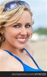 Close up portrait of a beautiful young blond woman with perfect teeth smiling while sitting on a beach