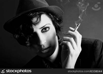 Close-up portrait of a brunette woman smoking a cigarette on black background wearing a hat