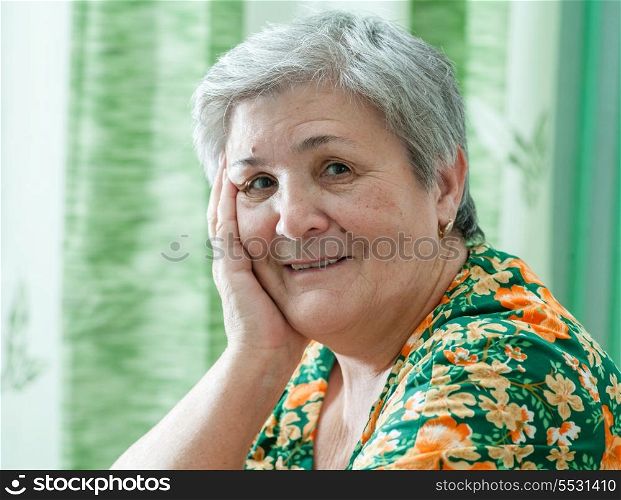 Close up portrait of a happy smiling senior woman resting her chin on her hands and looking directly at the camera