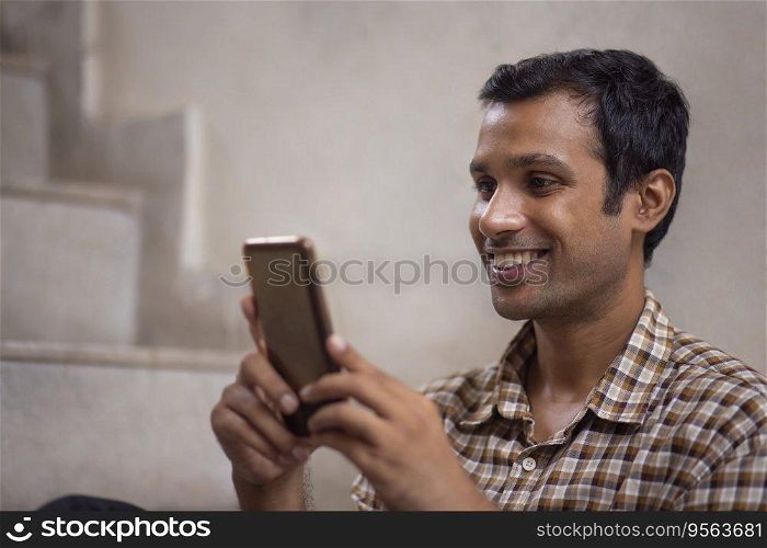 Close-up portrait of a happy young man using mobile phone