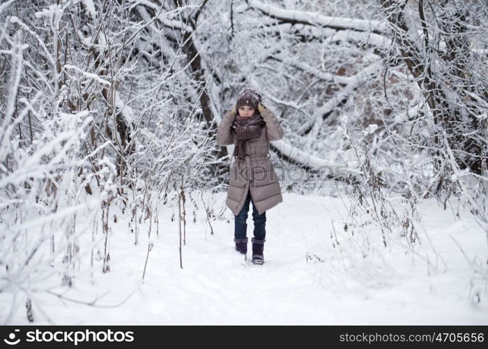 Close-up portrait of a little girl in brown jacket and knit scarf and hat on a background of a snow park