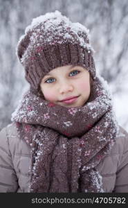 Close-up portrait of a little girl in brown jacket and knit scarf and hat on a background of a snow park