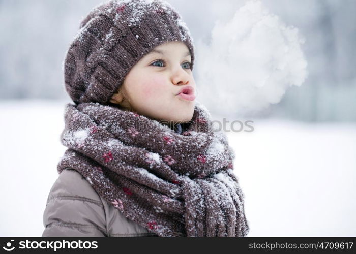 Close-up portrait of a little girl in brown jacket and knit scarf and hat on a background of a snow park