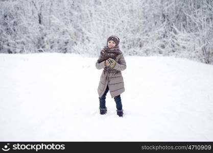 Close-up portrait of a little girl in brown jacket and knit scarf and hat on a background of a snow park