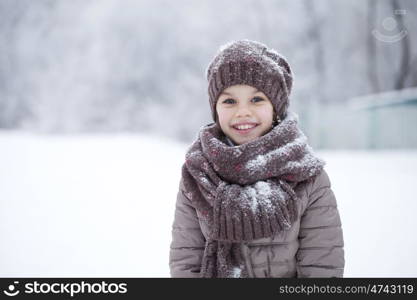 Close-up portrait of a little girl in brown jacket and knit scarf and hat on a background of a snow park