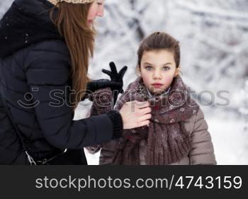 Close-up portrait of a little girl in brown jacket and knit scarf and hat on a background of a snow park