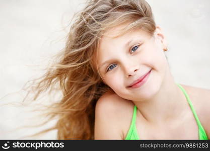 Close-up Portrait of a pretty little girl with waving in the wind long hair sitting on the beach