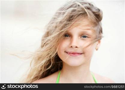 Close-up Portrait of a pretty smiling little girl with waving in the wind long hair sitting on the beach