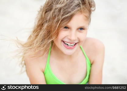 Close-up Portrait of a pretty smiling little girl with waving in the wind long hair sitting on the beach