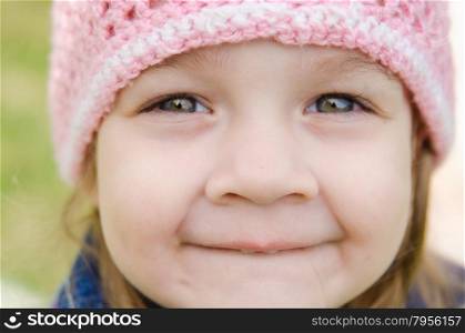 Close-up portrait of a smiling three-year girl. Close-up of a three-year girl with a cheerful smile in a pink hat