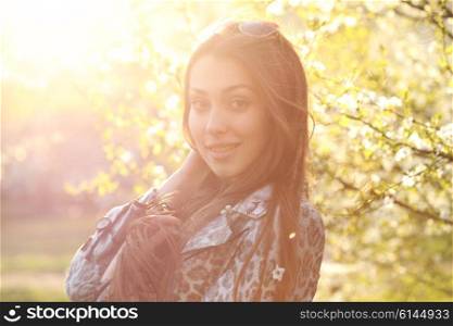 Close up portrait of a trendy woman at sunset standing outdoors in spring landscape background.