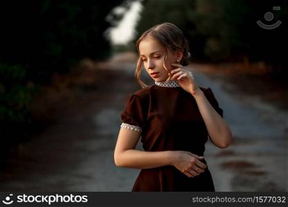close-up portrait of a young beautiful girl in a brown dress in a retro style on an abandoned road.