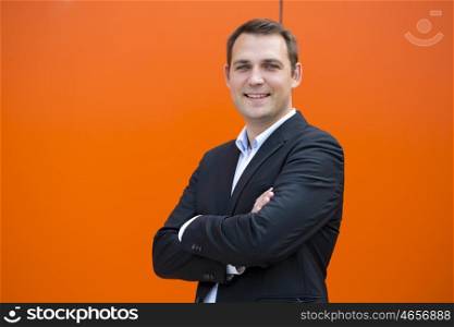 Close up portrait of a young business man in a dark suit and white shirt, against the backdrop of an orange wall