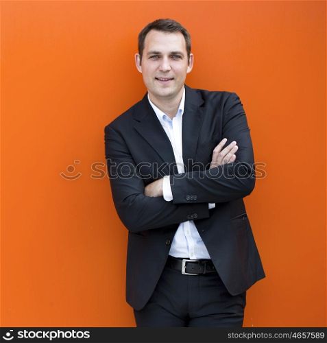 Close up portrait of a young business man in a dark suit and white shirt, against the backdrop of an orange wall