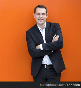 Close up portrait of a young business man in a dark suit and white shirt, against the backdrop of an orange wall