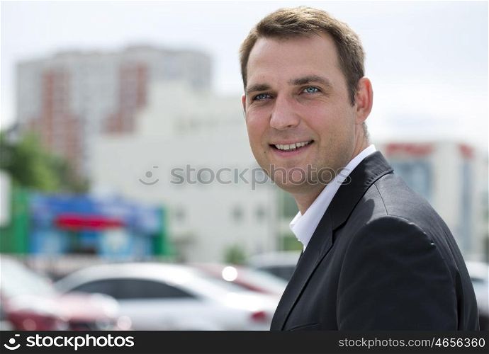 Close-up portrait of a young business man in a dark suit and white shirt on the background of summer city