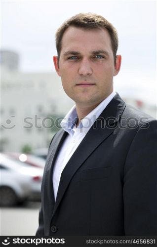 Close-up portrait of a young business man in a dark suit and white shirt on the background of summer city