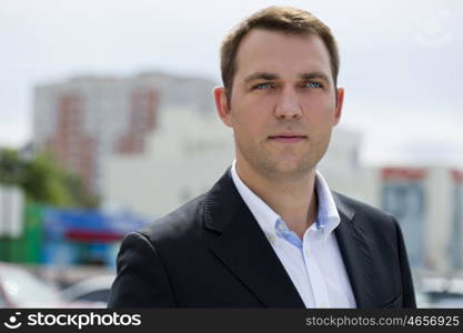 Close-up portrait of a young business man in a dark suit and white shirt on the background of summer city