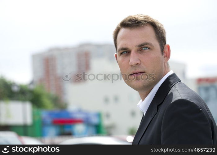 Close-up portrait of a young business man in a dark suit and white shirt on the background of summer city