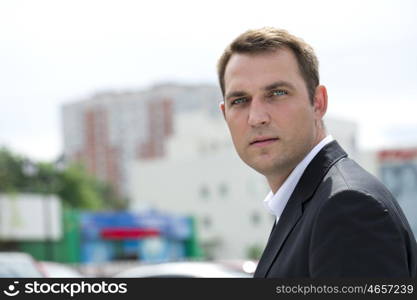 Close-up portrait of a young business man in a dark suit and white shirt on the background of summer city