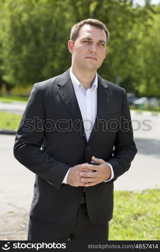 Close-up portrait of a young business man in a dark suit and white shirt on the background of summer city