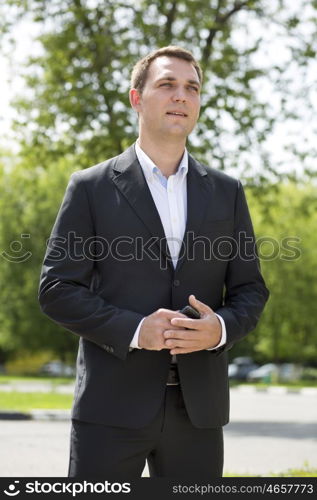 Close-up portrait of a young business man in a dark suit and white shirt on the background of summer city