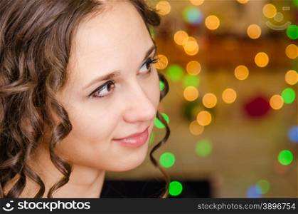 Close-up portrait of a young European girl against a blurred background of Christmas lights. Portrait of a girl looking to the right