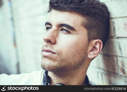 Close-up portrait of a young man with blue eyes posing near a wall. Model of fashion in urban background wearing white t-shirt