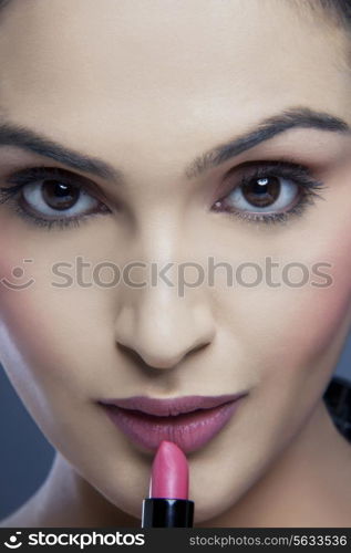 Close-up portrait of a young woman applying lipstick