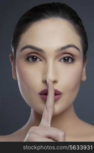 Close-up portrait of a young woman gesturing silence over colored background