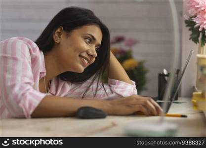 Close-up portrait of a young woman leaning on desk and using laptop