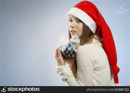 close-up portrait of adorable woman with long smooth hair, winter style and santa claus hat posing with blue bauble in the hand and looking in camera