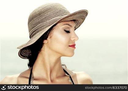 Close up portrait of an beautiful woman wearing sun hat on a tropical beach with her eyes closed
