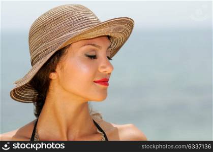Close up portrait of an beautiful woman wearing sun hat on a tropical beach with her eyes closed