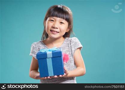 Close up portrait of asian little happy girl with blue present box , isolated on light blue background .