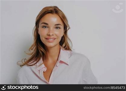 Close-up portrait of beautiful attractive blonde woman with shiny blue eyes and healthy skin in casual shirt looking straight at camera pleasantly smiling, isolated over grey studio background. Close-up portrait of beautiful attractive blonde woman with shiny blue eyes, in casual shirt
