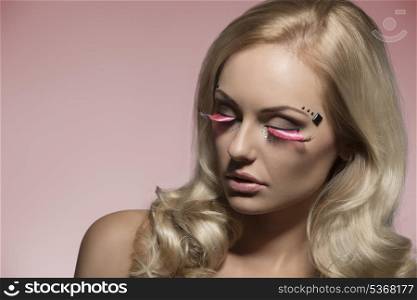 close-up portrait of beautiful blonde girl with pink creative feathered shiny make-up, long wavy silky hair and perfect visage skin