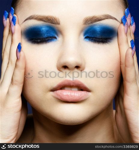 Close-up portrait of beautiful brunette with blue eye shadow make up and manicure