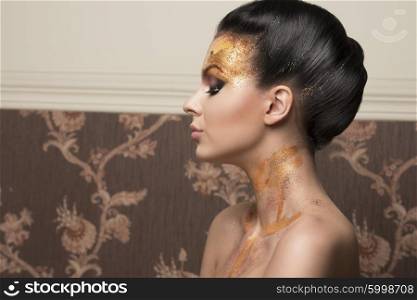close-up portrait of beautiful brunette woman with creative hair-style and artistic shiny golden christmas make-up, turned on profile with naked shoulders