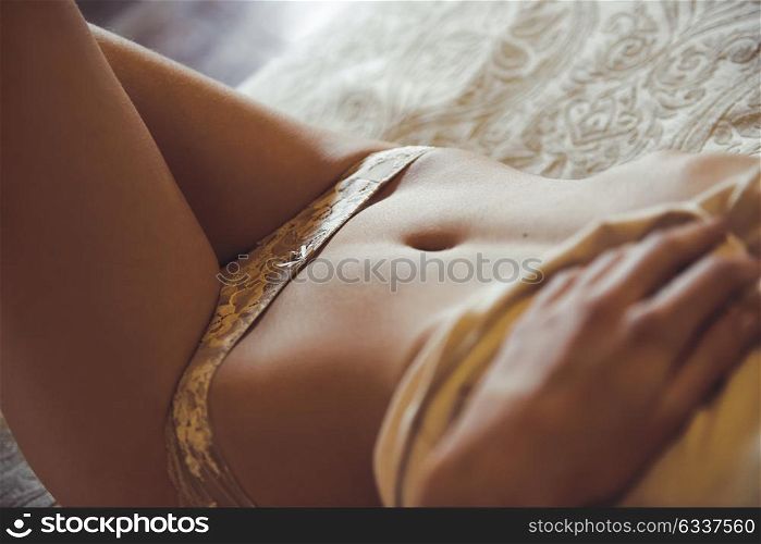 Close-up portrait of beautiful woman in lingerie posing on the bed of her bedroom. Girl wearing white panties and casual t-shirt