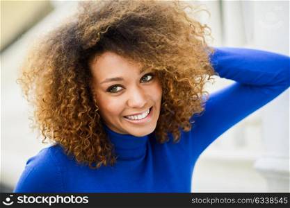 Close-up portrait of beautiful young African American woman, model of fashion, smiling with afro hairstyle and green eyes wearing blue sweater in urban background